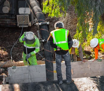Two workers in high-visibility gear daylighting a buried utility with a hydrovac hose